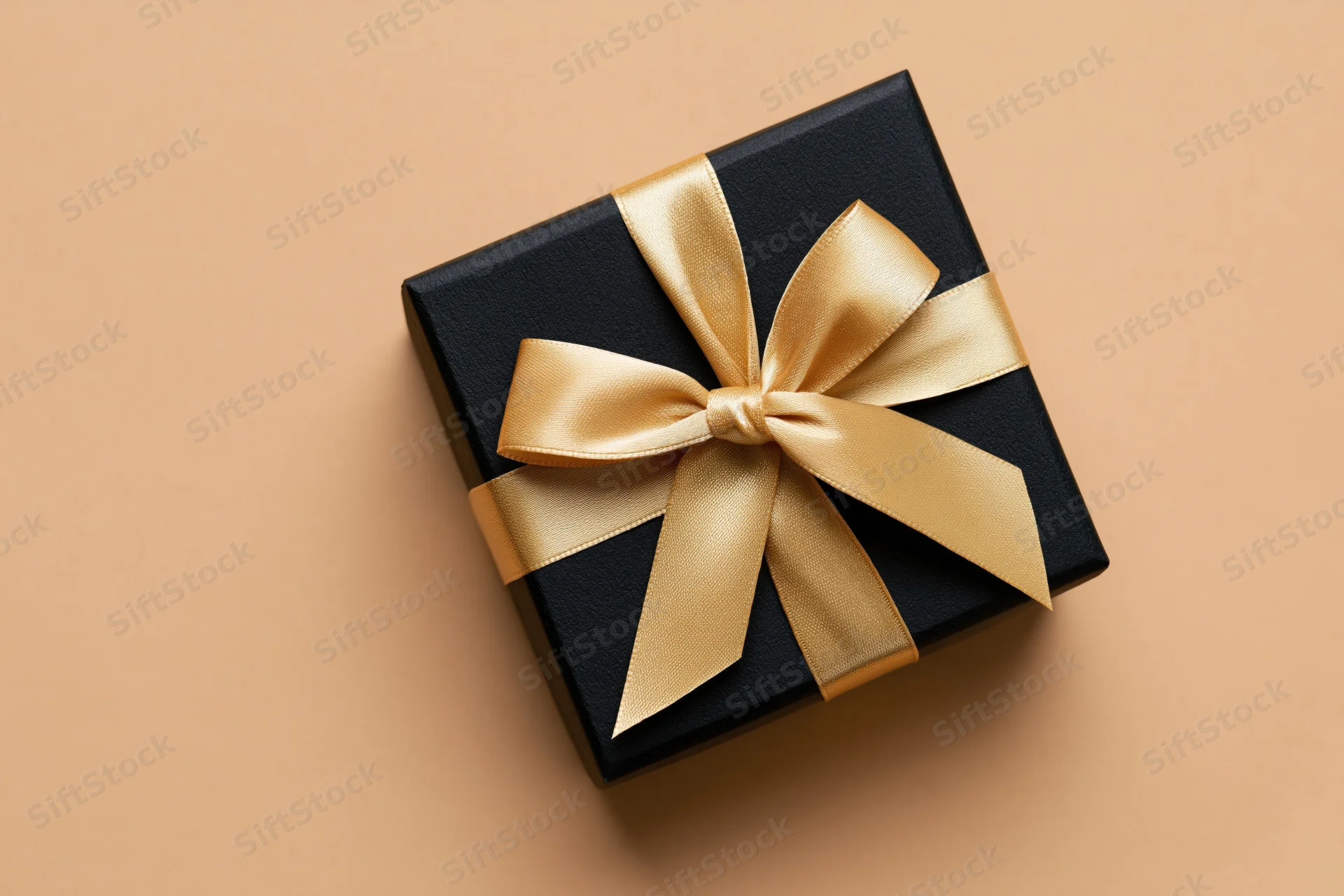 Black gift box with gold satin ribbon bow on beige surface