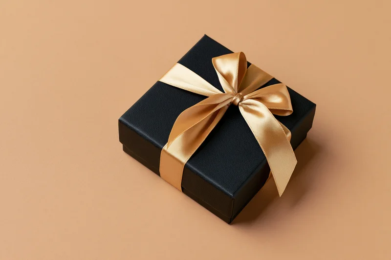 Black gift box wrapped with gold satin ribbon on beige surface