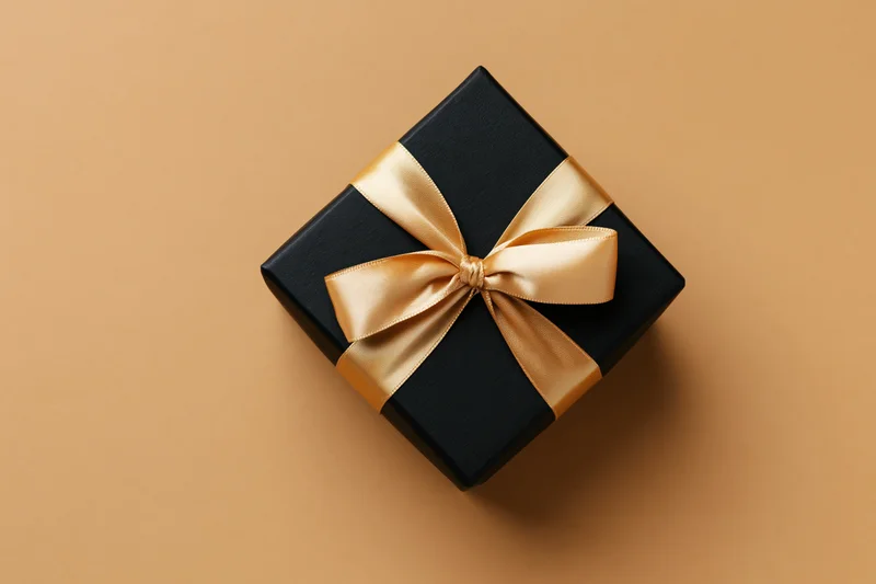 Black gift box with gold satin ribbon bow on beige surface