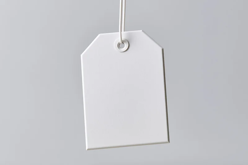Blank white paper tag hanging from string against gray background