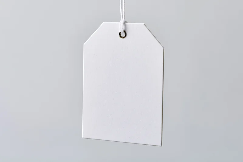 Blank white paper tag hanging from string against plain background