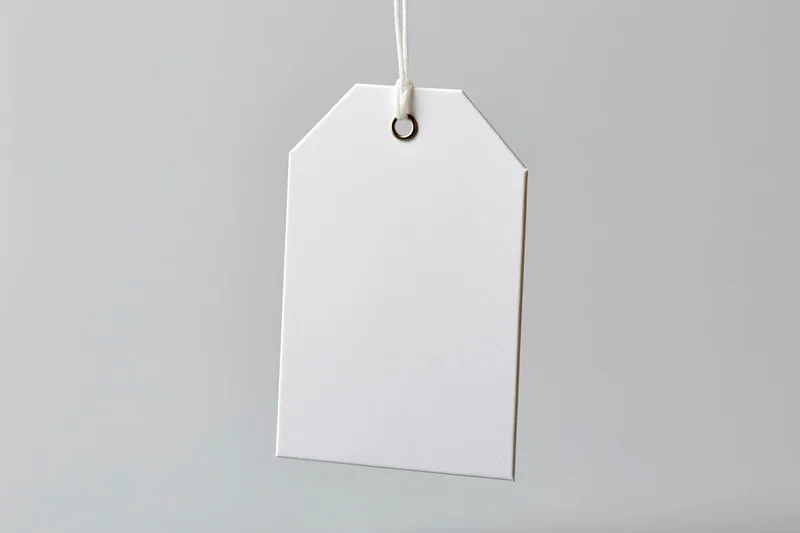 Blank white paper tag hanging from string against plain background