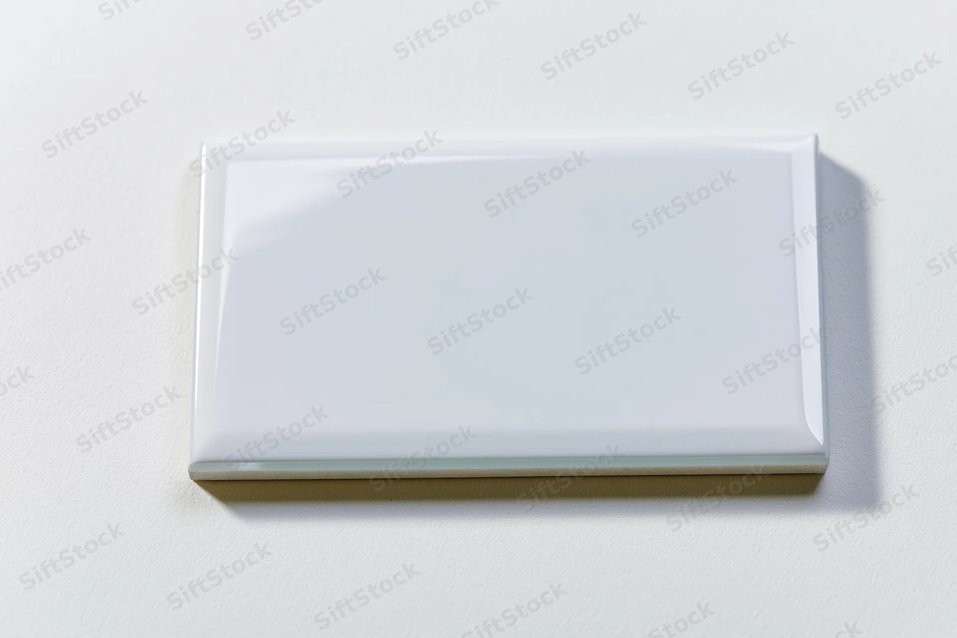 Blank white rectangular glass tile lying flat on a smooth white surface