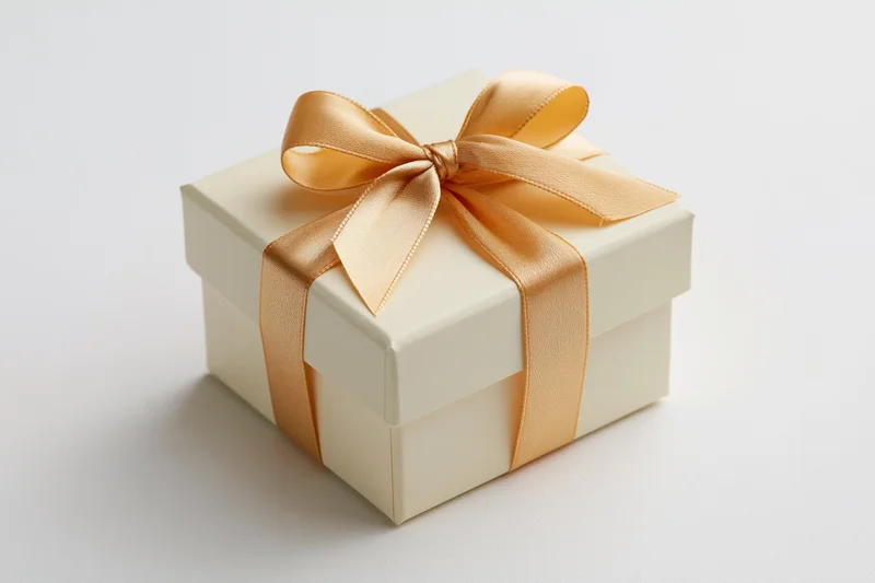 Cream gift box with gold satin ribbon bow on white background