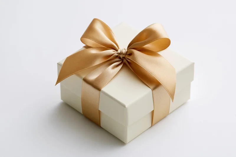 Cream gift box with gold satin ribbon bow on white background