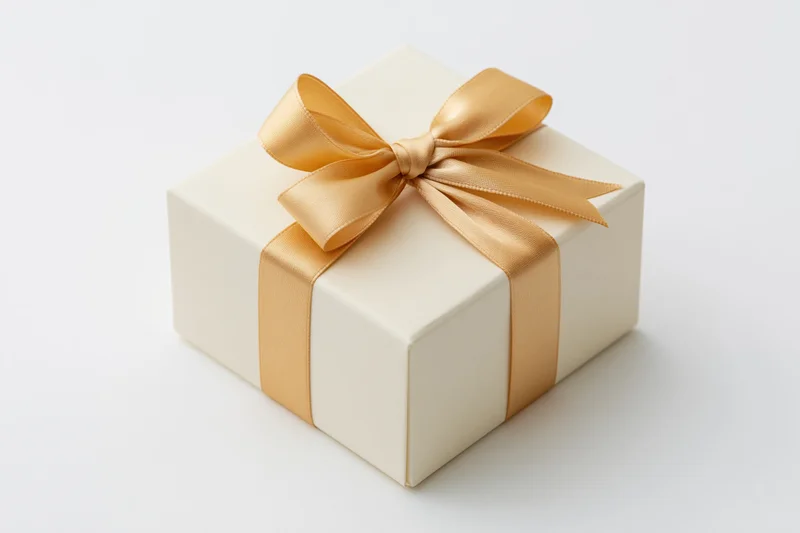 Cream gift box with gold satin ribbon bow on white background