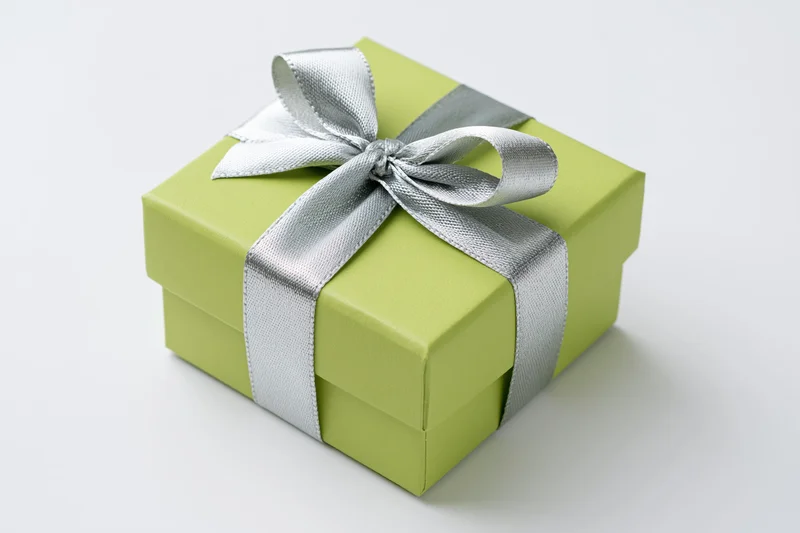 Green gift box with silver ribbon and bow on white surface