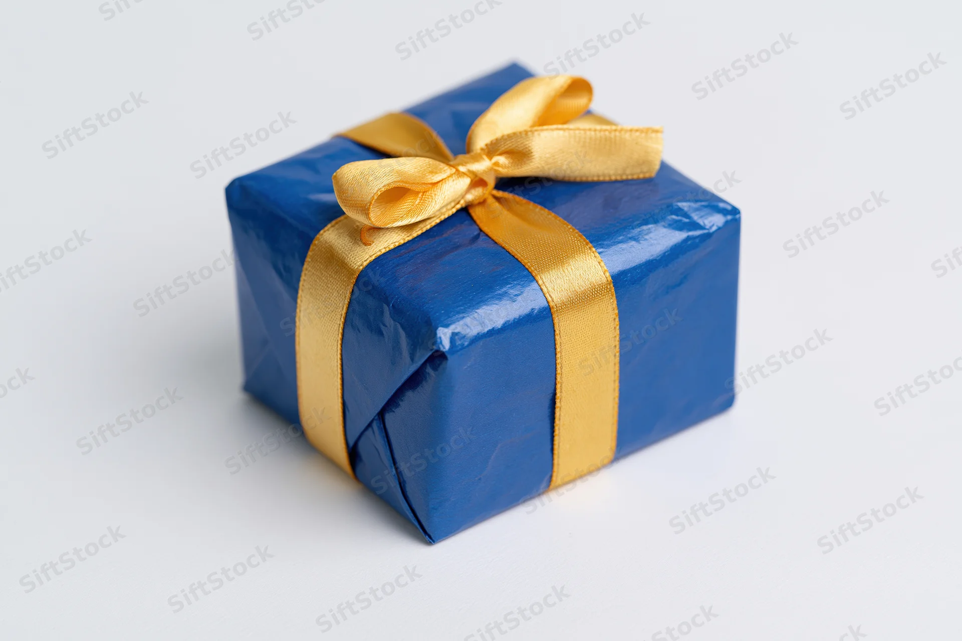 Blue gift box wrapped in glossy paper with gold ribbon bow on white surface