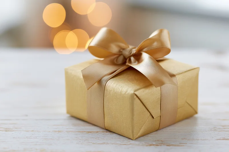 Gold gift box wrapped with ribbon and bow on wooden surface with bokeh lights in background