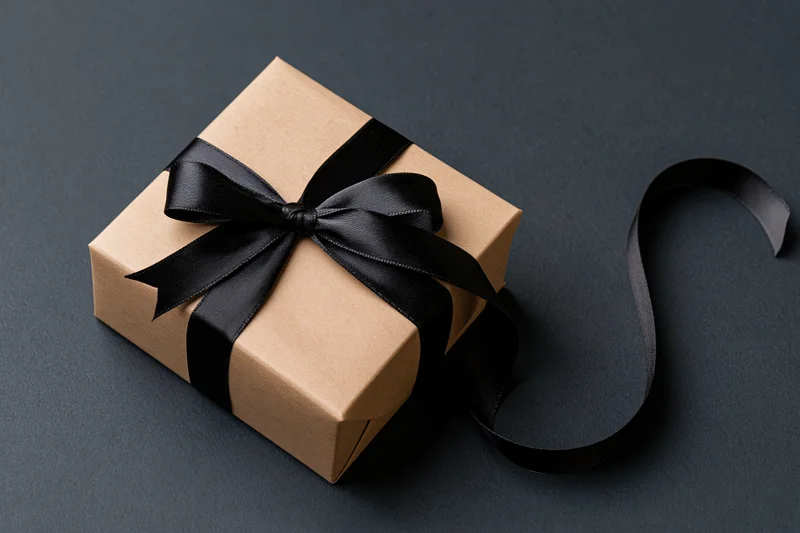 Gift box wrapped in kraft paper with black ribbon bow on dark surface