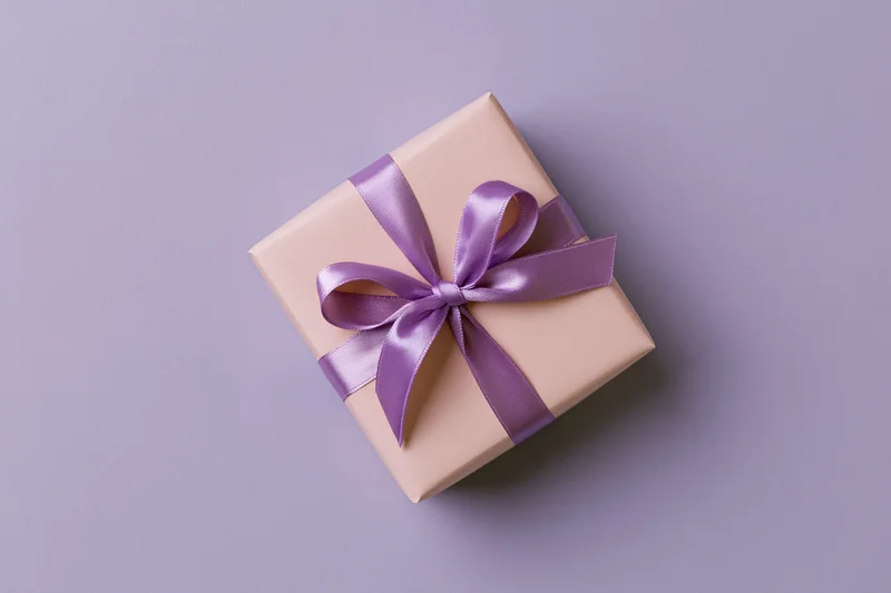 Gift box wrapped in blush pink paper with purple satin ribbon on lavender background