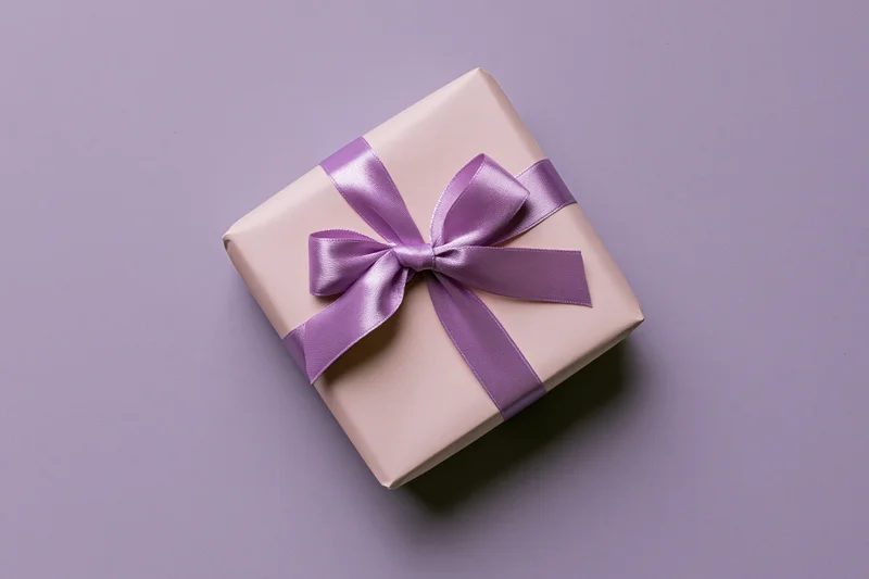 Gift box wrapped in pale pink paper with purple satin ribbon on purple surface