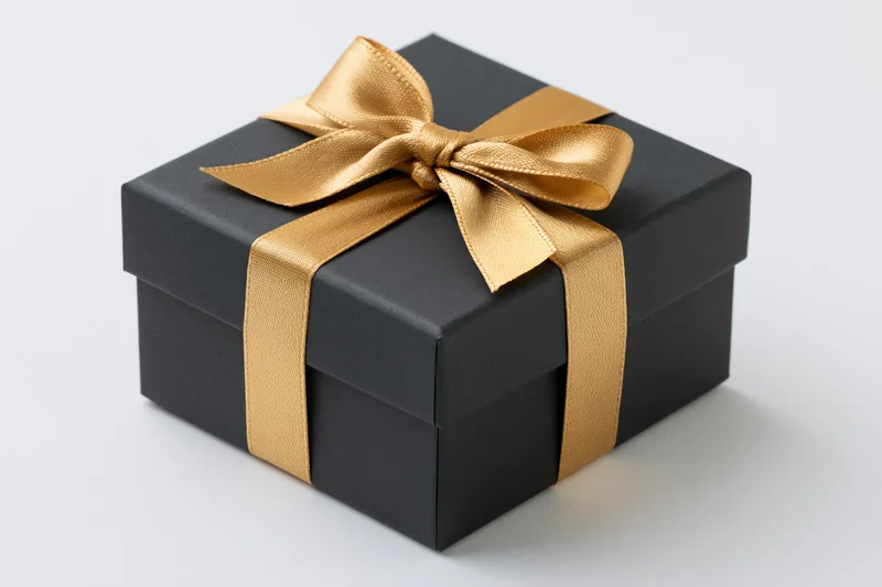 Matte black square gift box wrapped with gold satin ribbon on white background