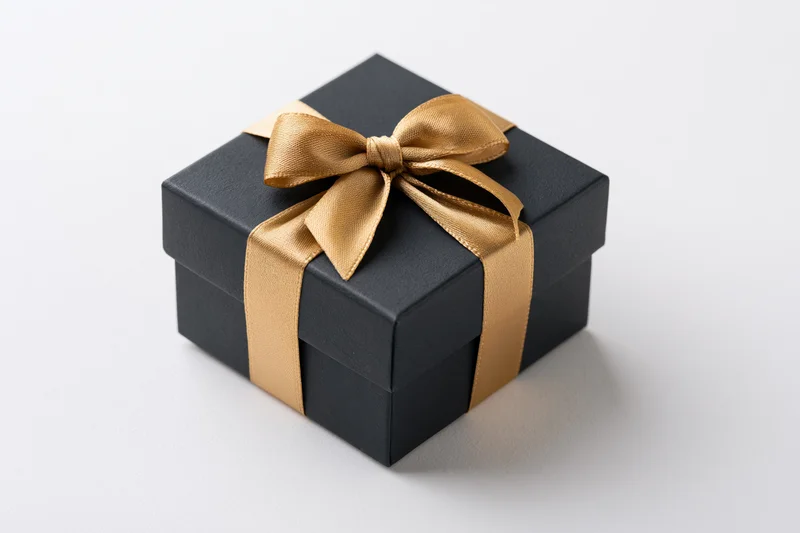Matte black square gift box with gold satin ribbon bow on white surface