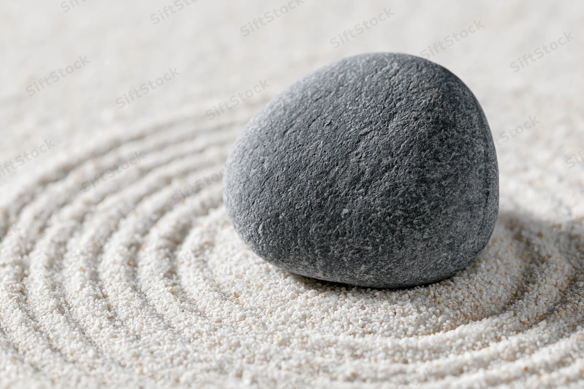 Smooth grey stone resting on raked white sand with concentric patterns