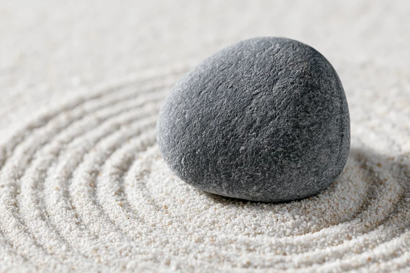 Smooth grey stone resting on raked white sand with concentric patterns