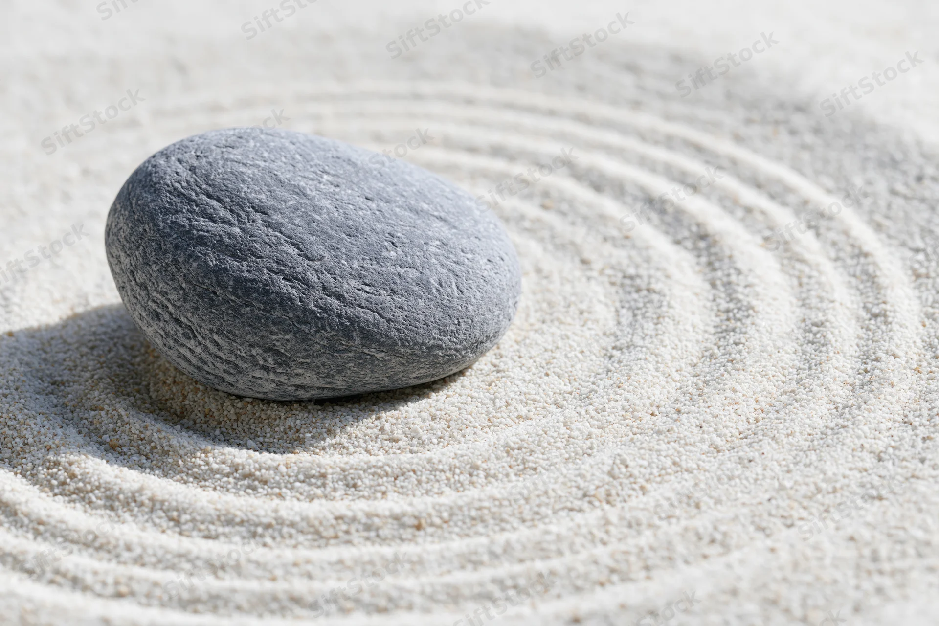 Smooth grey stone resting on finely raked white sand in a zen garden