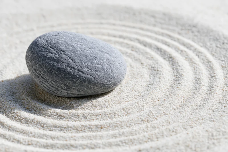 Smooth grey stone resting on finely raked white sand in a zen garden