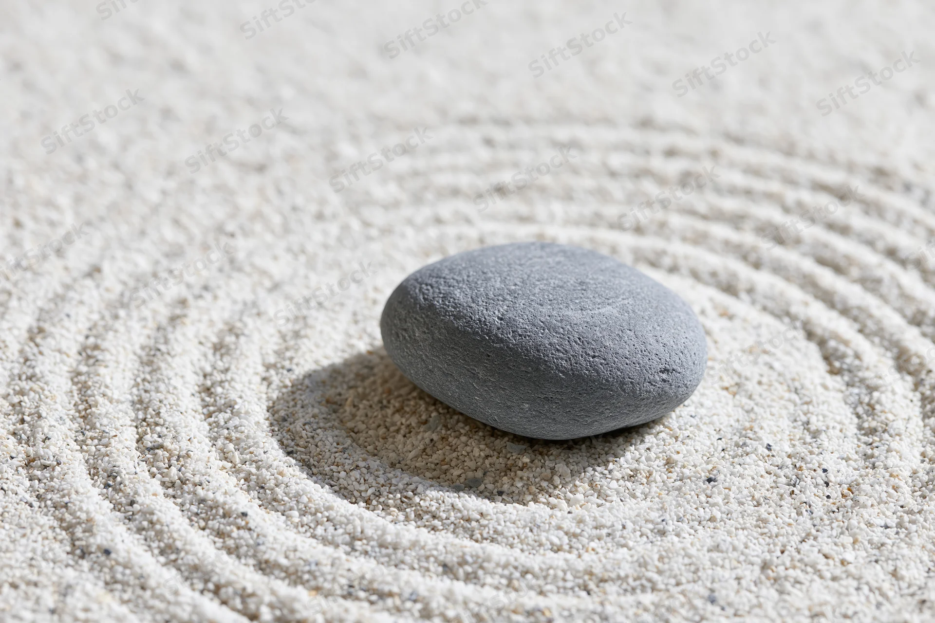 Smooth grey stone resting on finely raked white sand in concentric circles