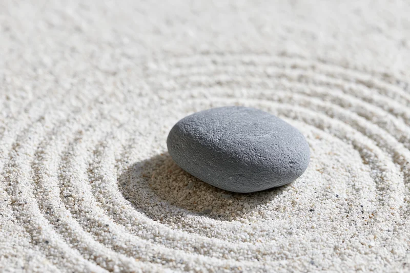 Smooth grey stone resting on finely raked white sand in concentric circles