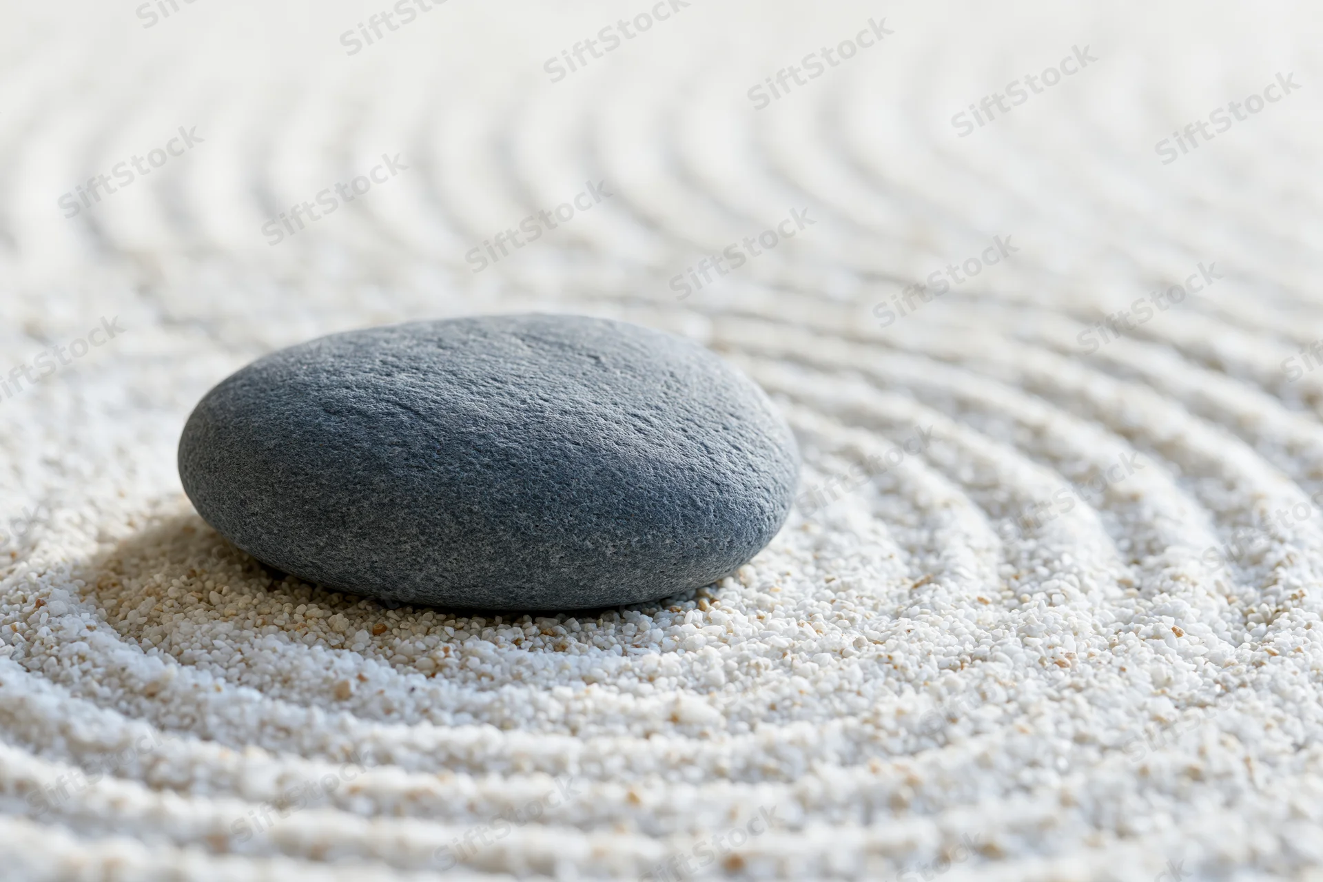 Smooth grey stone resting on finely raked white sand in concentric circles