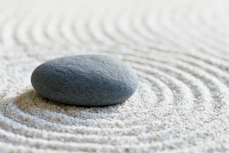 Smooth grey stone resting on finely raked white sand in concentric circles