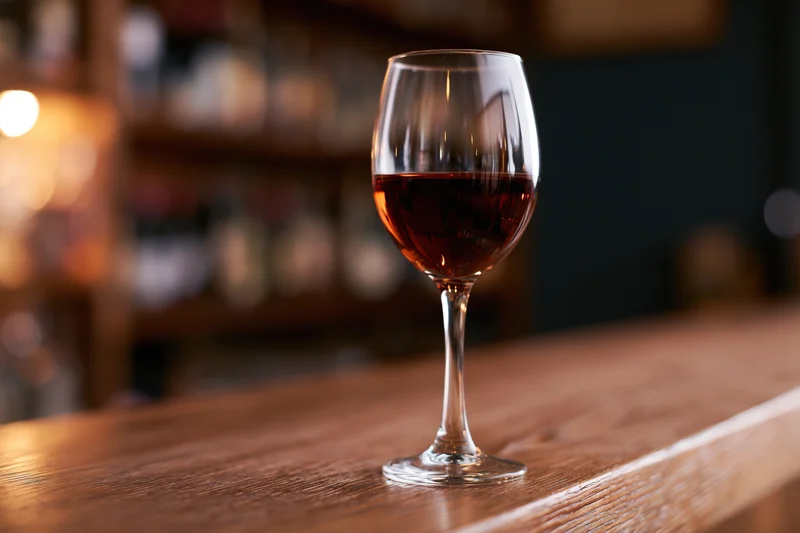 A stemmed wine glass half-filled with red wine on a wooden bar counter in a dimly lit restaurant