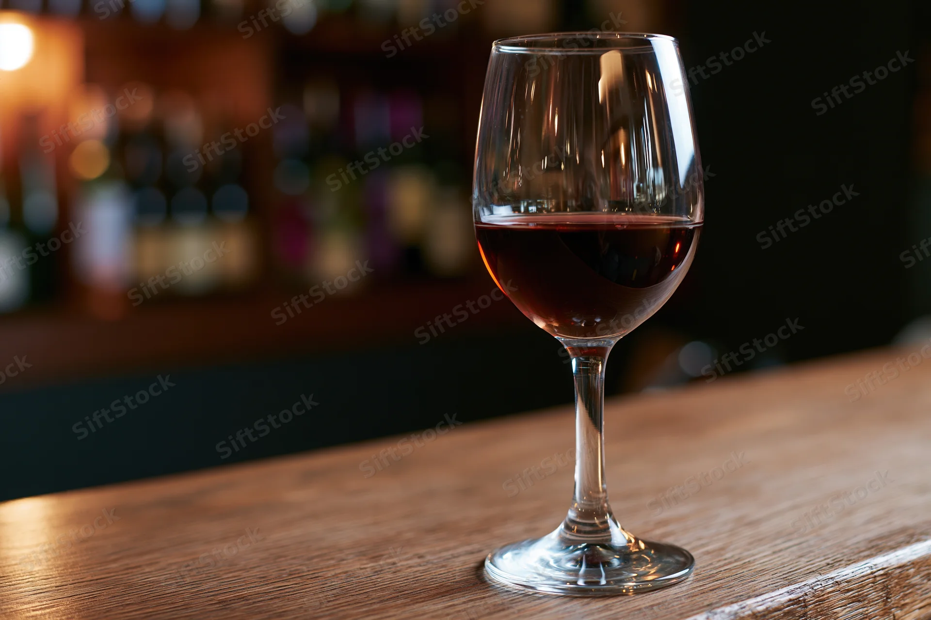 Half-filled red wine glass on wooden bar countertop in dimly lit restaurant interior