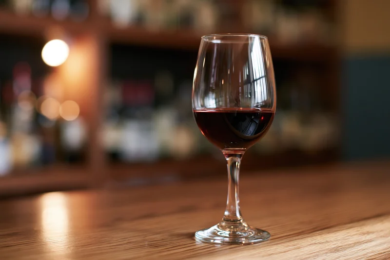Wine glass half-filled with red wine on wooden bar table in dimly lit restaurant