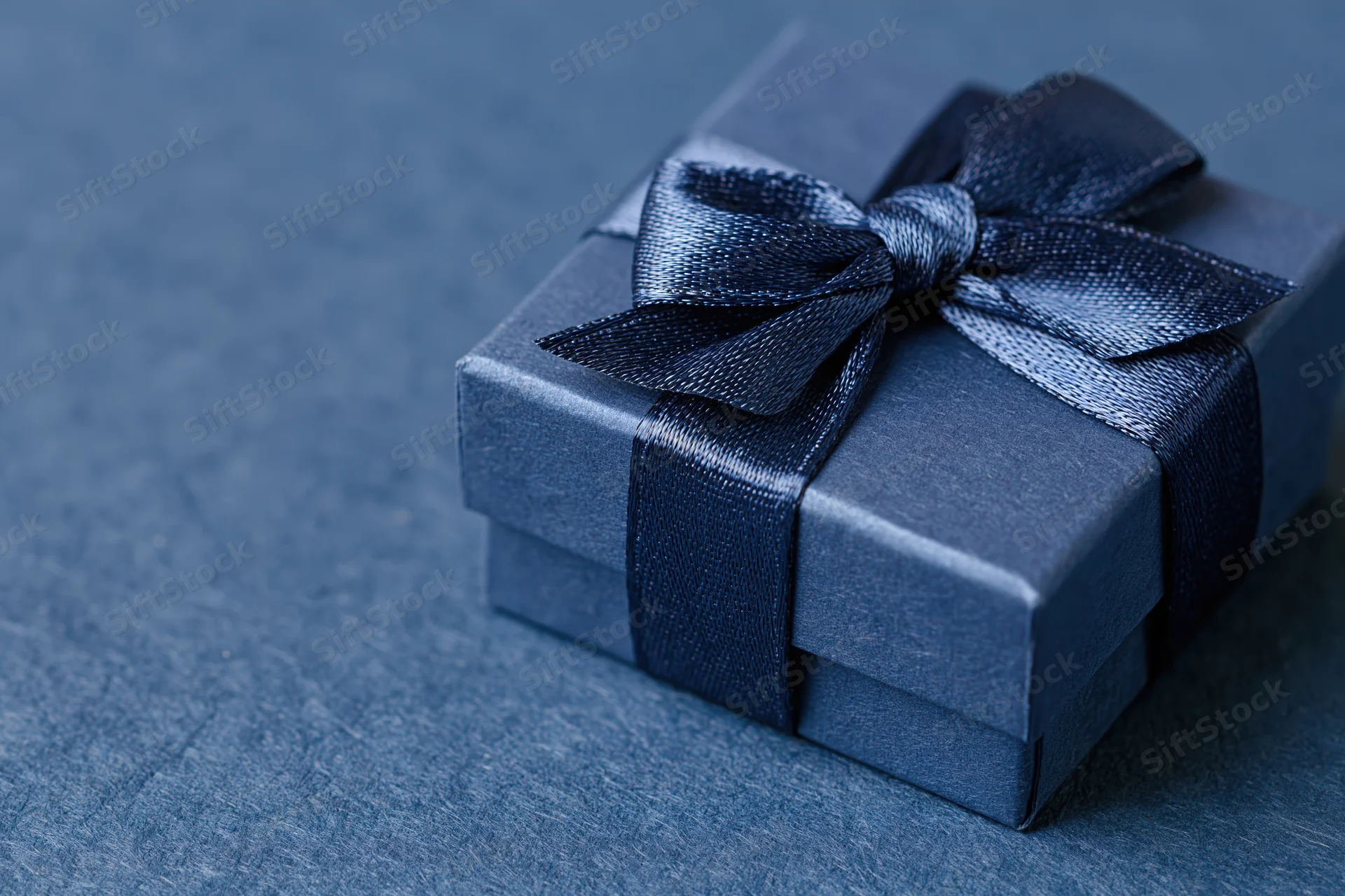 Small navy blue gift box wrapped with satin grosgrain ribbon on textured surface