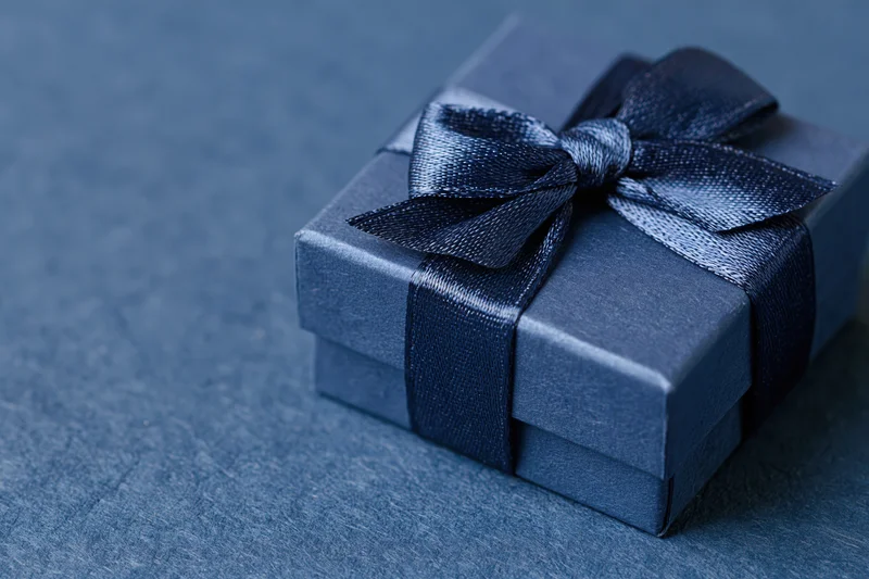 Small navy blue gift box wrapped with satin grosgrain ribbon on textured surface