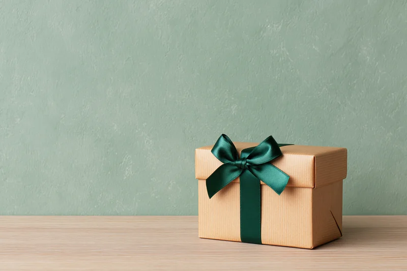 Small gift box wrapped in kraft paper with green ribbon on wooden table