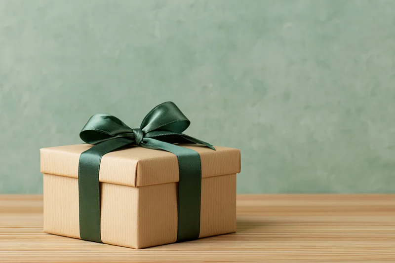 Small gift box wrapped in kraft paper with green ribbon bow on wooden table
