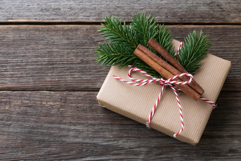 Small gift wrapped in kraft paper with cinnamon sticks and pine sprig on wooden surface