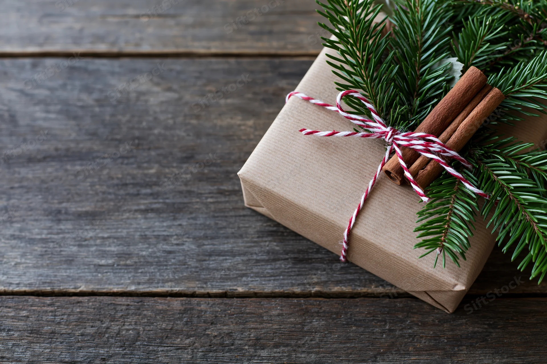 Gift box wrapped in kraft paper with cinnamon sticks and pine branch on wooden table