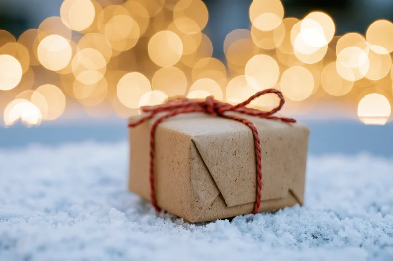 Small kraft paper gift box tied with red twine resting on snow with blurred golden lights behind