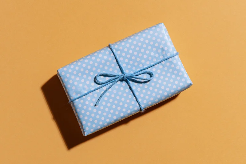 Small rectangular gift box wrapped in light blue polka dot paper with twine bow on orange background