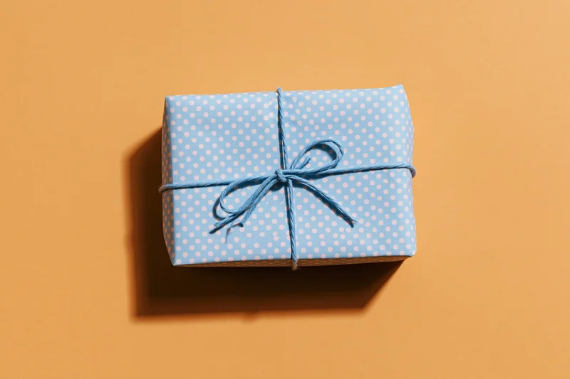 Small rectangular gift box wrapped in light blue polka dot paper with twine bow on orange background