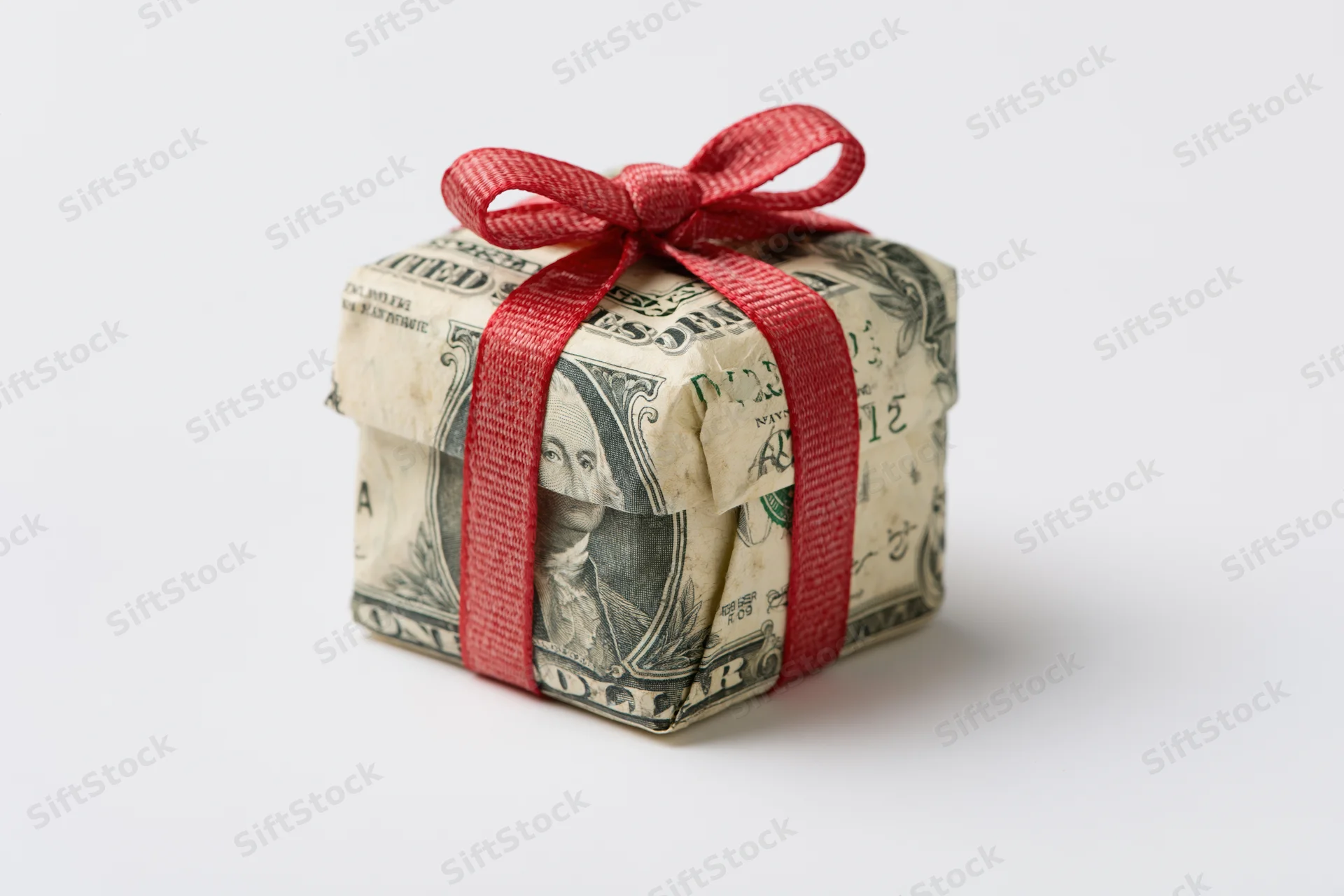 Small gift box wrapped in us dollar bills with red ribbon on white background