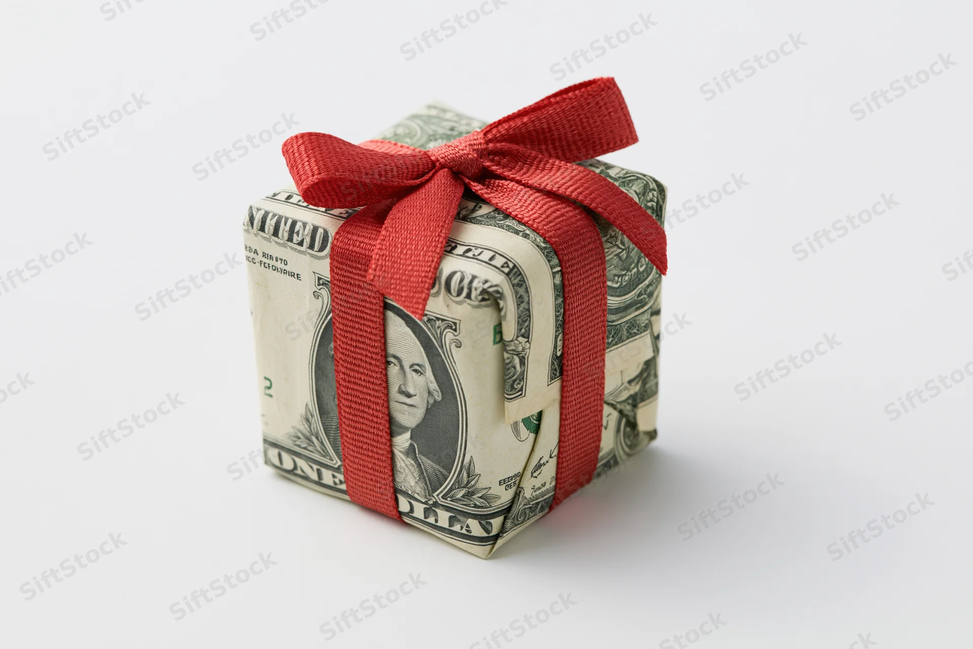Small gift box wrapped in us dollar bills with red ribbon on white background