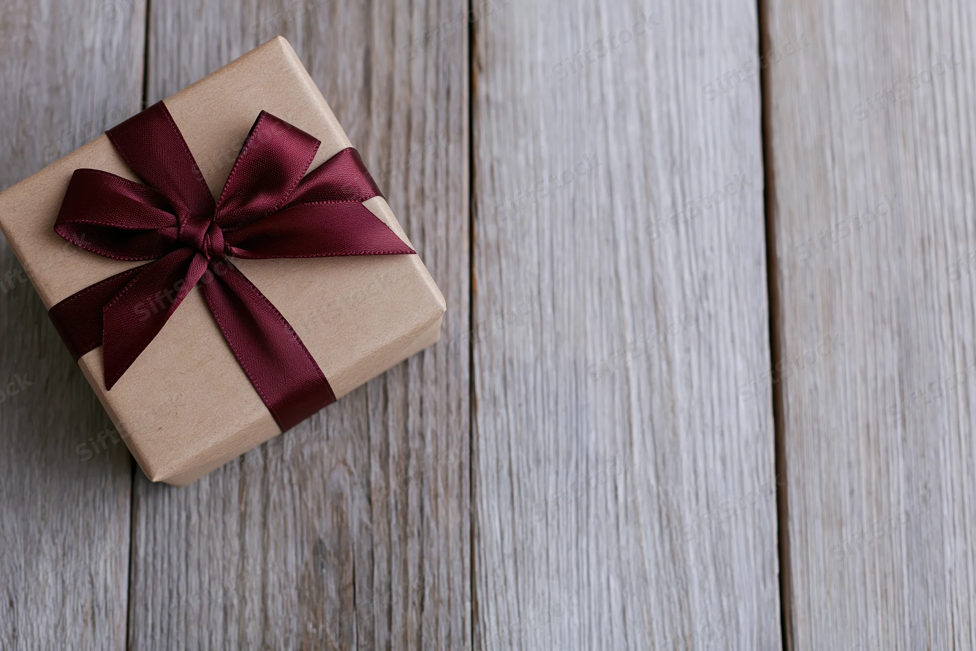 Small gift box wrapped in kraft paper with burgundy ribbon bow on wooden surface