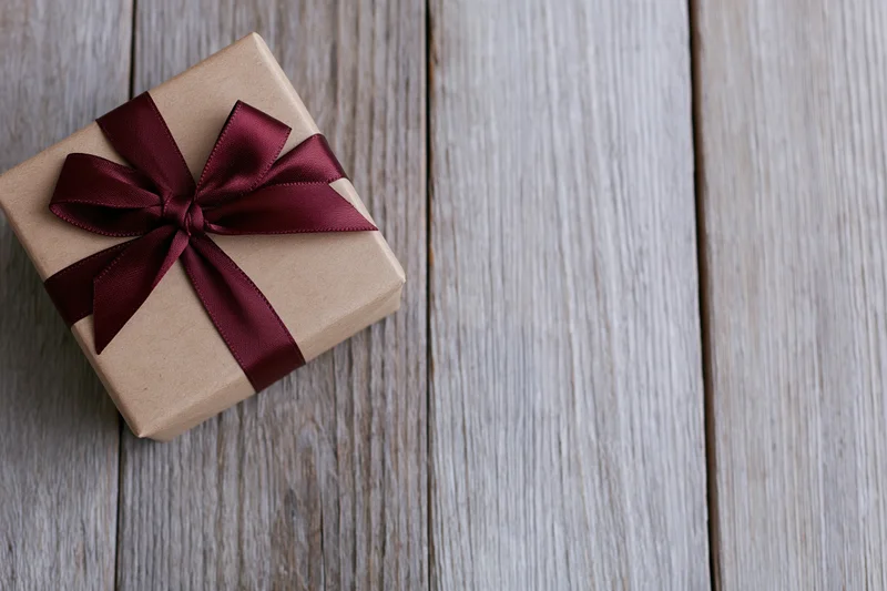 Small gift box wrapped in kraft paper with burgundy ribbon bow on wooden surface