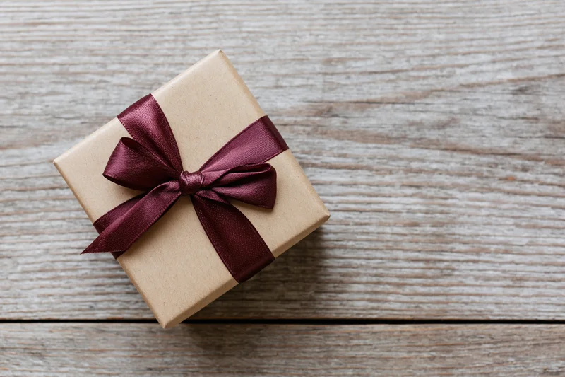 Small gift box wrapped in kraft paper with burgundy ribbon bow on wooden surface