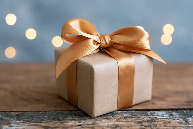 Small gift box wrapped in kraft paper with gold ribbon bow on wooden table