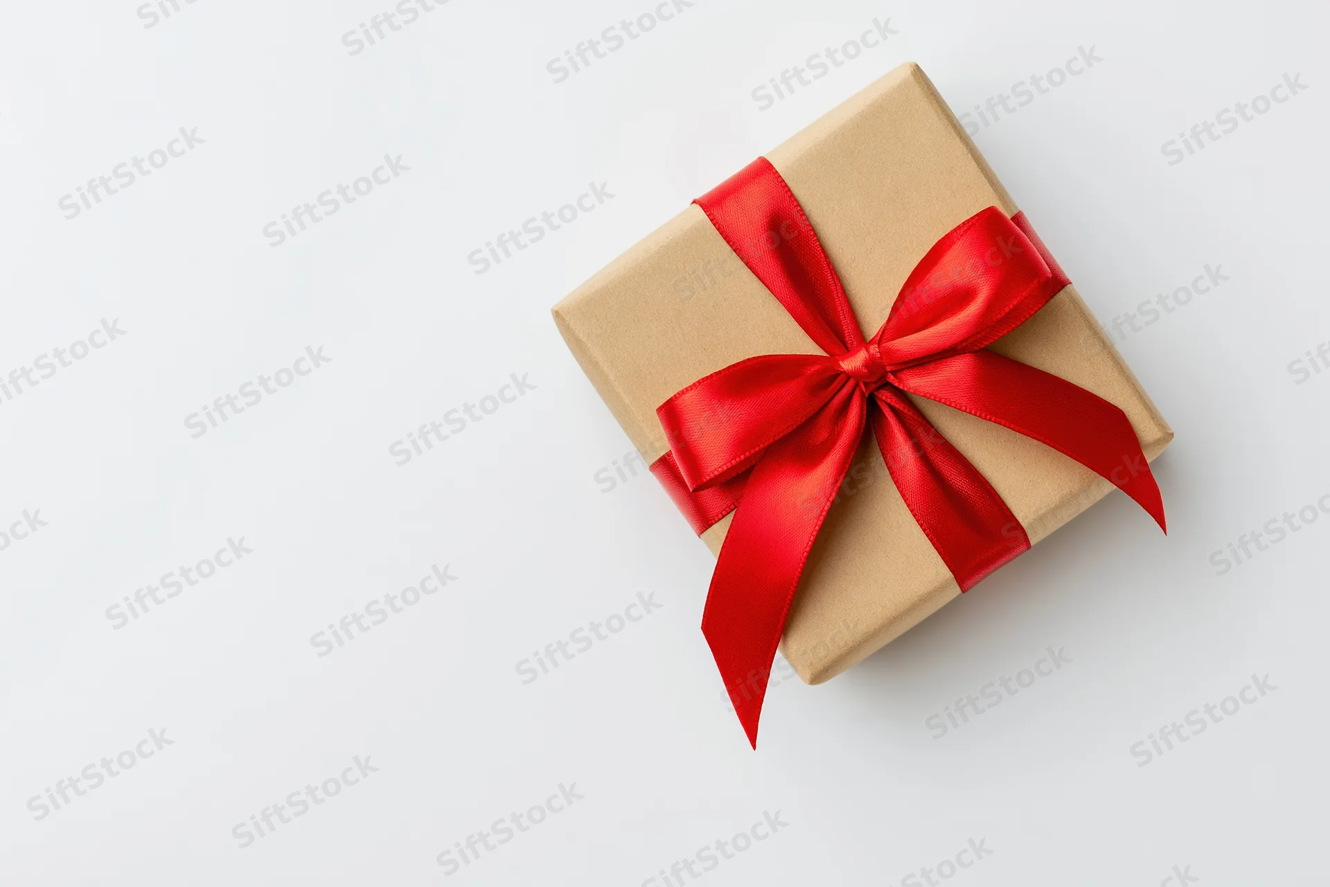 Small square gift box wrapped in kraft paper with red ribbon bow on white background