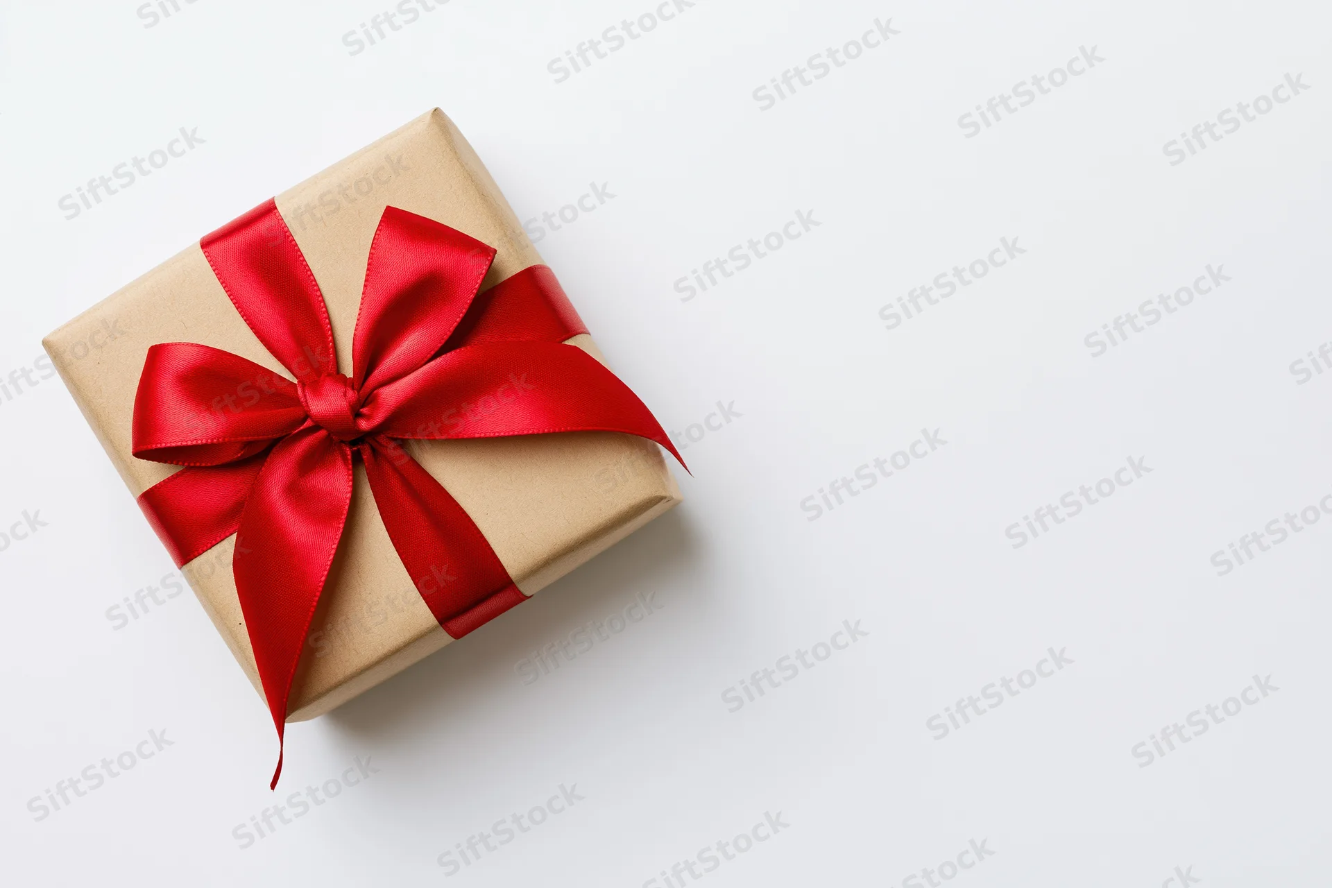 Small square gift box wrapped in kraft paper with red ribbon bow on white surface