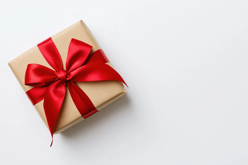 Small square gift box wrapped in kraft paper with red ribbon bow on white surface