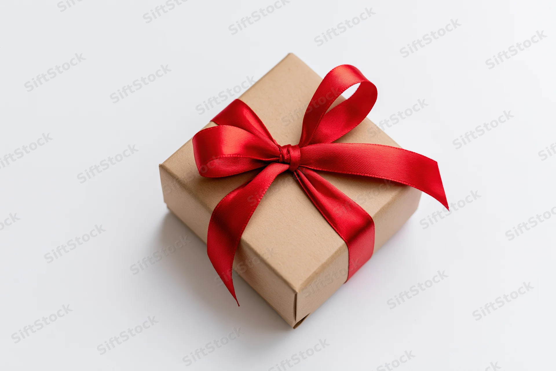 Small square gift box wrapped in brown paper with red satin ribbon bow on white background
