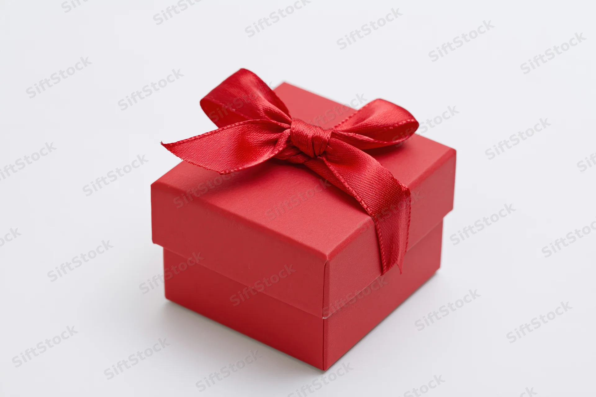 Small red gift box with a satin ribbon bow on white background