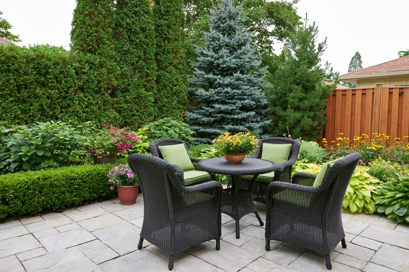 Dark wicker patio furniture set on stone paving surrounded by garden plants and shrubs